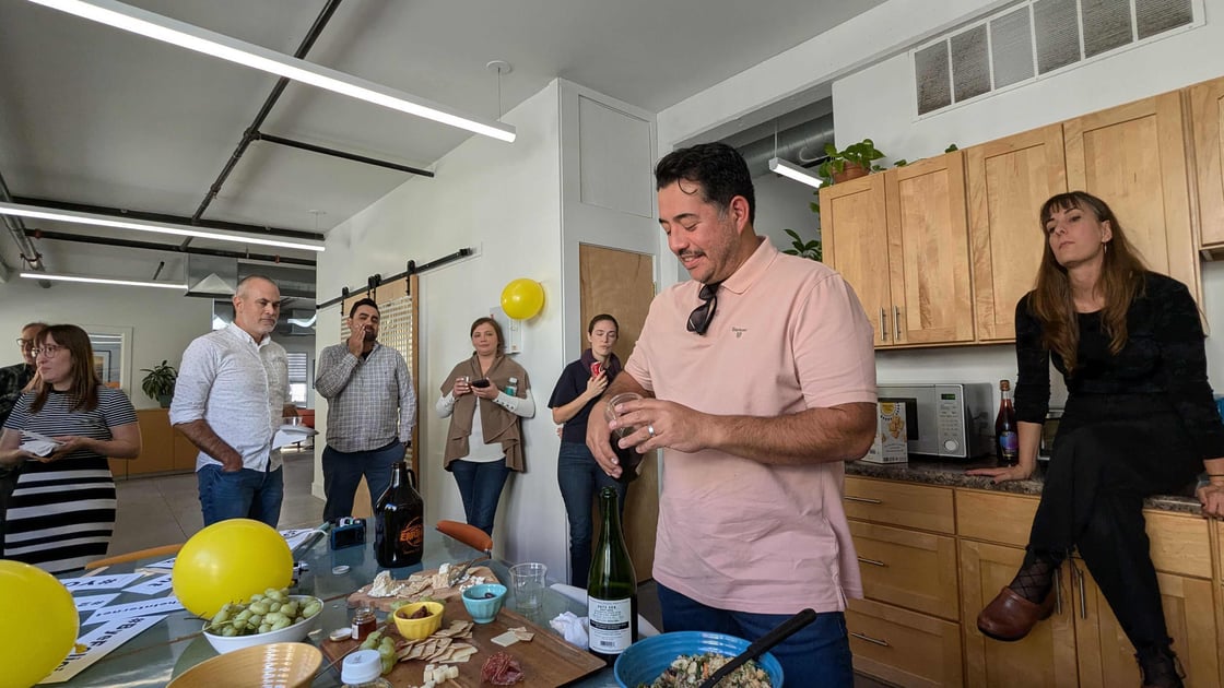 fernando meza pouring champagne while coworkers gather in the oneupweb kitchen